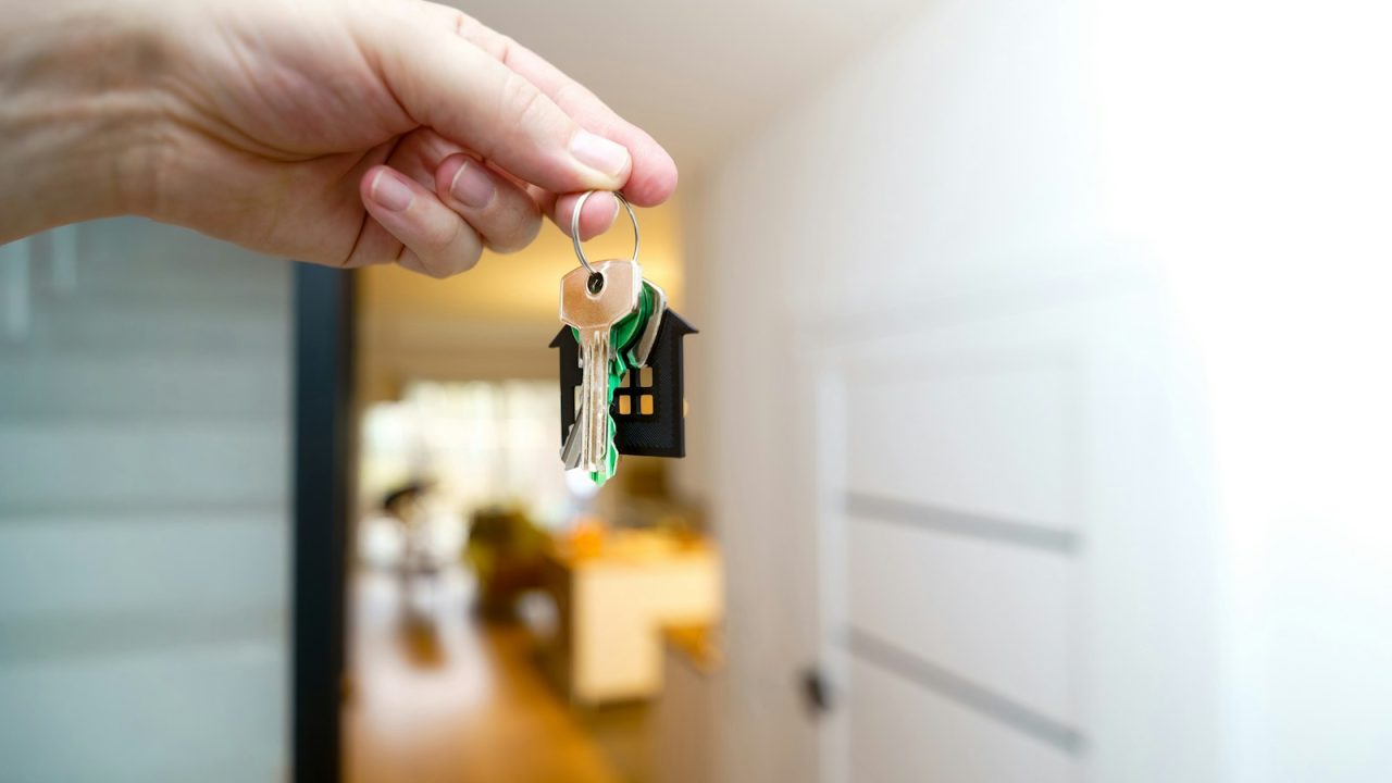 A hand holding a set of house keys in front of the entrance to a home