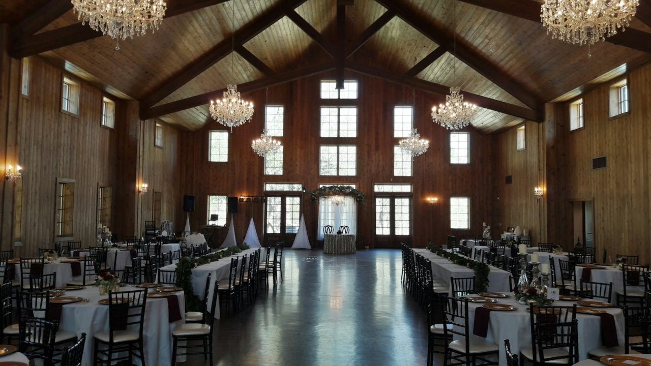 Rustic wedding reception venue with wooden beams, crystal chandeliers, and long tables set for guests